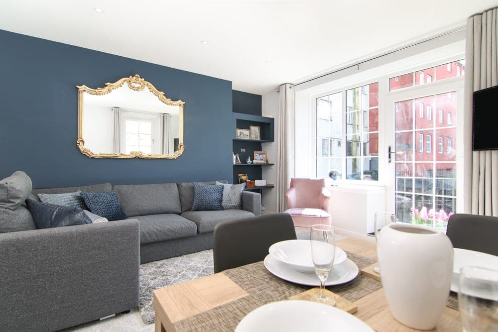 Living room with navy feature wall, gilt mirror and corner sofa